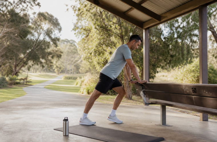 Runner performing supported calf and ankle mobility beside a park bench